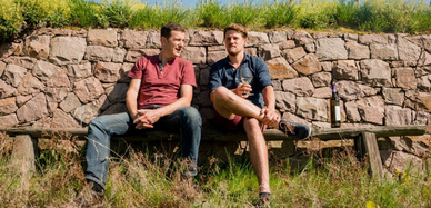 Martin Schwarz und Matthias Schuh auf einer Bank bei einem Glas Wein