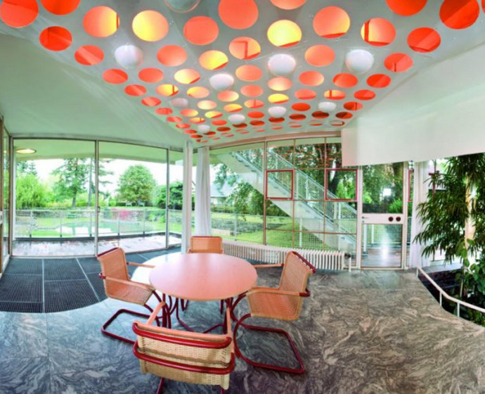 Dining table surrounded by glass walls with red lighting above.