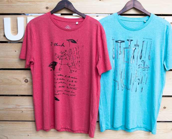 Zwei T-Shirts mit unterschiedlichen Motiven hängen an der Wand